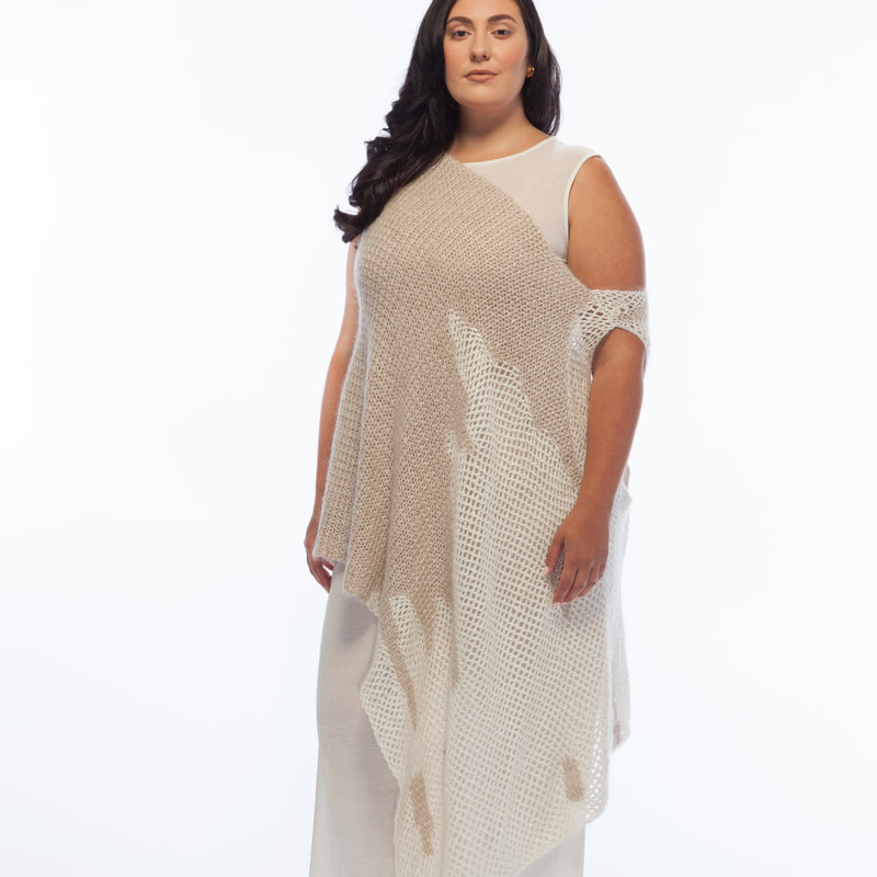 Curve model, Sarah, is pictured against a white wall, wearing LISA AVIVA's Column Dress, in Cream - topped with the Hand Crocheted Poncho in Baby Camel and Cream.
